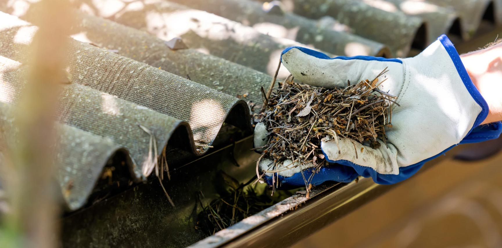 A gloved hand diligently clearing debris from a rooftop gutter in Salem, showcasing meticulous attention to detail.
